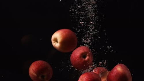 Rote Äpfel gießen auf schwarzem Hintergrund ins Wasser, Früchte fallen ins Wasser, Zeitlupe