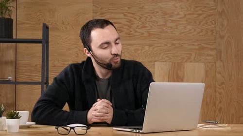 Smiling Casual Young Man with Headset Using Computer in a Bright Office