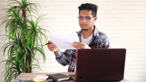 Young Asian Man Analyzing Data on Paper Working on Desk