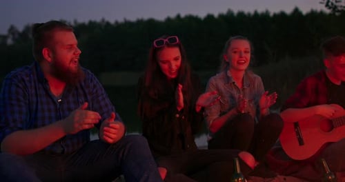 Friends Sing Around a Campfire at Night