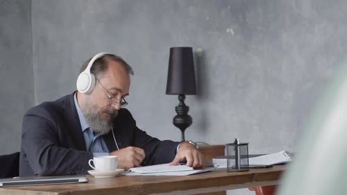 Man Wearing Headphones Writing at Modern Desk