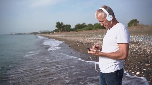 Man Listening to Music on Beach Using Phone