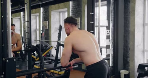 Muscular Man Leans on Equipment in Gym