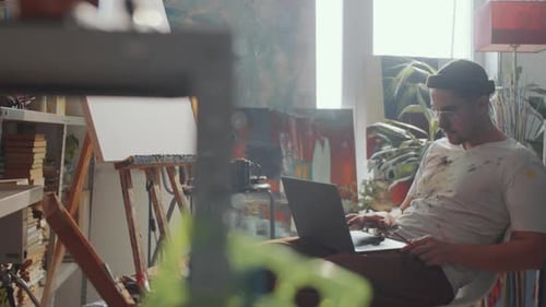 Man Drinking Tea and Using Laptop in Art Studio