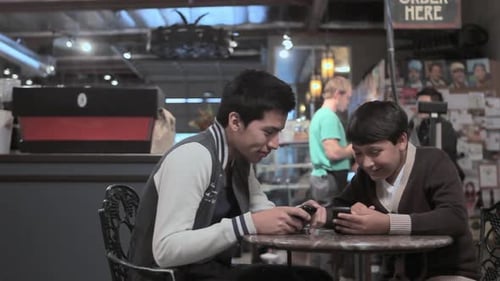 Two brothers with smartphones in cafe