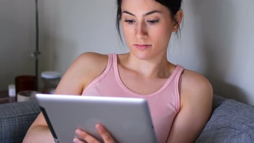 Young Adult Uses Tablet at Home on Couch