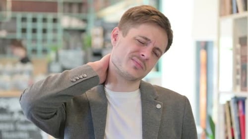 Young Adult Man Massaging Stiff Neck Indoors