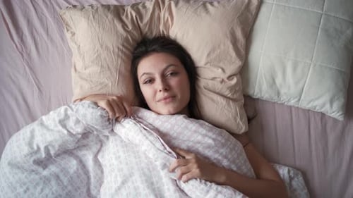 Top View of a Young Attractive Woman Stretching Hands While Lying in Bed in the Morning
