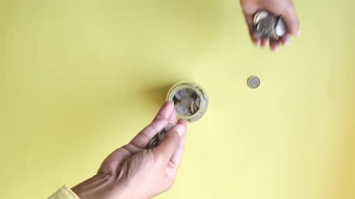 Hand Deposits Coins in Jar for Saving