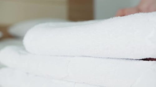 Closeup of Hands Putting Stack of Fresh White Bath Towels on the Bed in Hotel Room