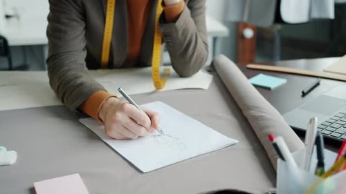 Nahaufnahme männlicher Hände, die ein neues modisches Kleidungsstück skizzieren, während der Designer im Studio arbeitet