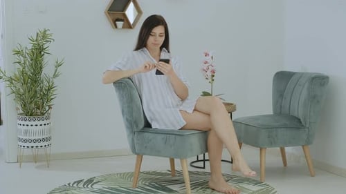 Woman Sitting in Armchair Using Mobile Phone