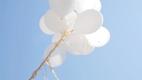White Balloons with Gold Ribbons Floating in Sky
