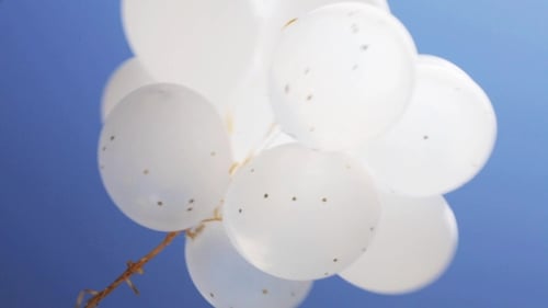 Swirling White Balloons Against Blue Sky Background