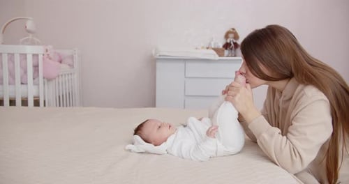Mother's Affectionate Kiss to Infant's Foot in Bedroom