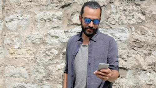 Young Adult Using Mobile Phone by Stone Wall