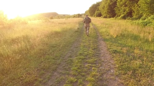 Aerial View: Soldier Goes On Path In The Field. Camera Behind Him