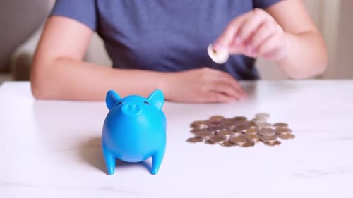 Woman's hand putting coins into blue piggy bank. Finance concept