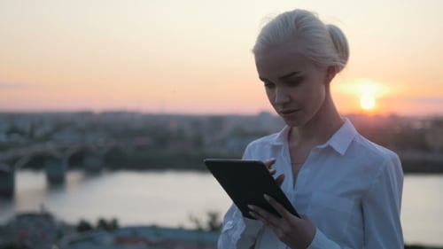 Woman Uses Tablet Device During Sunset Over City