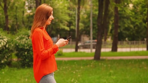Side View Ginger Woman Walking on the Street Holding Smartphone