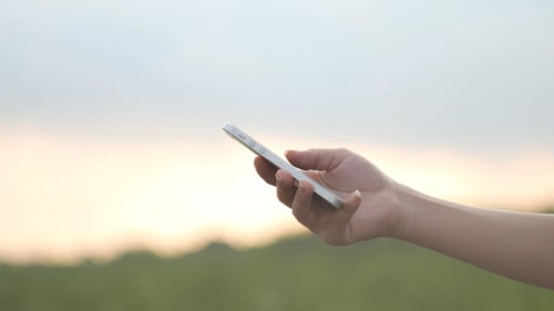 Hand Holding Phone Outdoors at Sunset