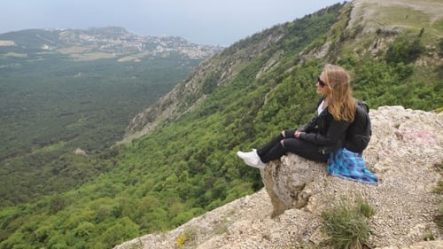 Woman Traveler Looks At The Edge Of The Cliff On The Sea Bay Of Mountains In The Background