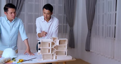 Young Architects With Model of a House Standing in Office