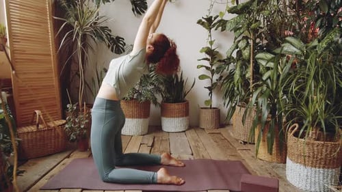 Mujer practicando yoga en postura de camello sobre colchoneta de fitness en casa
