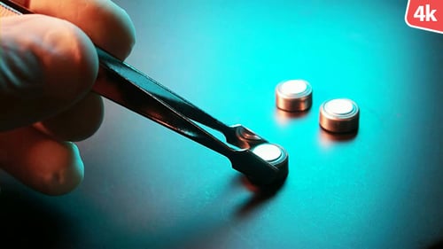 Tweezers Picking Up a Button Cell Battery