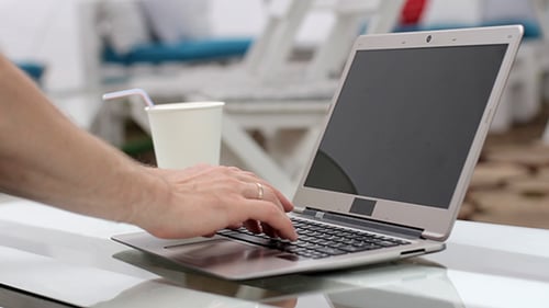 Hands Typing on Laptop Keyboard at Outdoor Cafe
