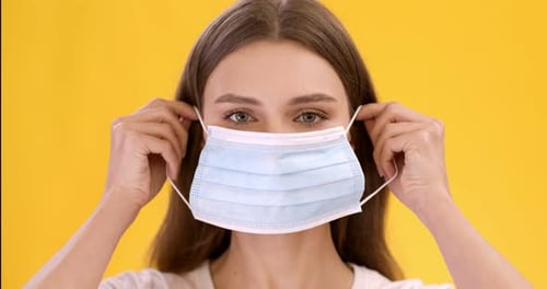 Woman Putting on a Blue Surgical Mask Close-Up