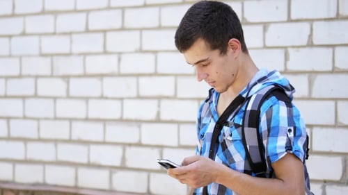 The Young Man is Typing a Message on a Smartphone