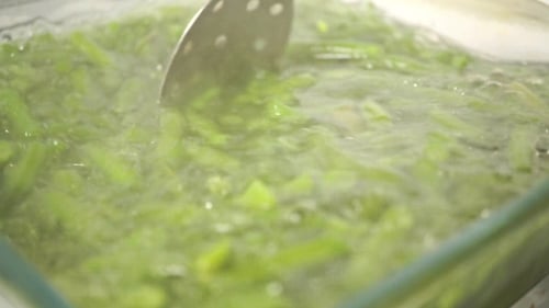 Mixing Boiling Green Beans With a Perforated Spoon