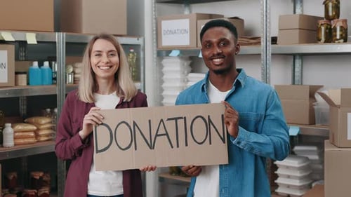 Smiling Volunteers Hold Donation Sign in Warehouse Setting
