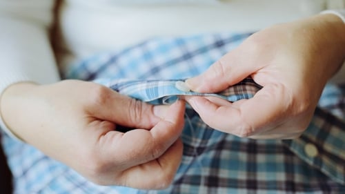 The Woman Sews a Button To a Plaid Shirt