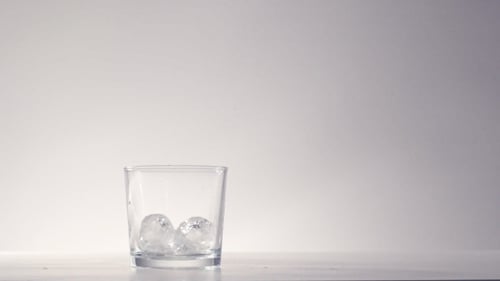 Golden Liquid Being Poured Over Ice Cubes