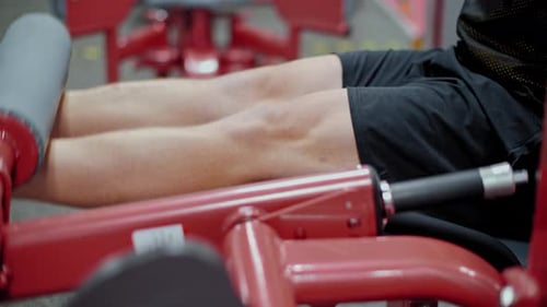 Atleta masculino treinando músculos das pernas no treinador de pesos no clube de ginástica. Treinamento de fisiculturista masculino em