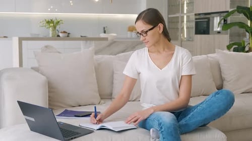 Woman Working on Couch With Laptop and Notebook