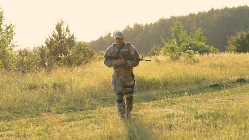 Military Man With Automaton In Hands Goes On The Path. Slowly