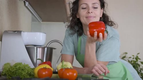 Woman Smells Fresh Red Pepper in Kitchen