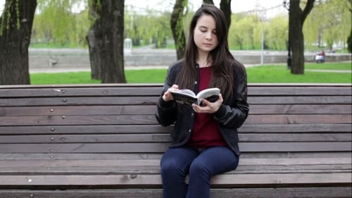 Woman Reads Book on Park Bench in City