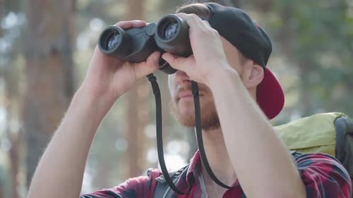 Nahaufnahme eines selbstbewussten gutaussehenden Mannes, der durch ein Fernglas im Freien schaut. Portrait von Bearded