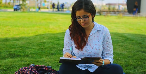 Young Woman Writing in Notebook on Green Grass