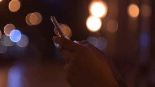 Hand Swiping on Phone at Night with Bokeh