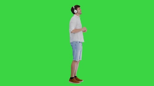 Casual Young Man in Headphones Listening To Music and Enjoying It on a Green Screen, Chroma Key.