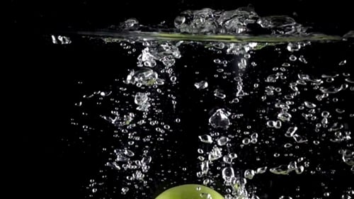 Les pommes vertes tombent dans l'eau sur fond noir