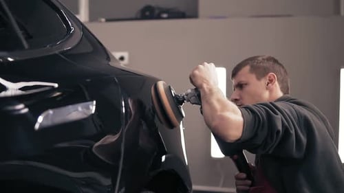 Man Polishing Black Car with Buffer in Garage
