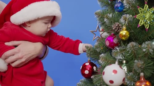 Baby in Santa Suit Touches Christmas Tree Ornament