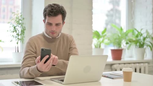 Man Using Smartphone While Using Laptop in Office