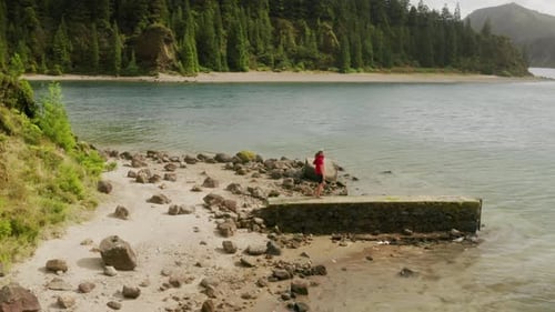 Un homme portant un t-shirt rouge observe un magnifique lac avec des montagnes volcaniques derrière